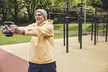 Glücklicher älterer Mann beim Training mit der Kettlebell im Park - UUF26073