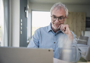 Senior freelancer wearing eyeglasses working on laptop at home - UUF26087