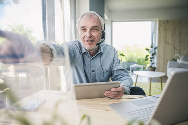 Freelancer wearing headset touching transparent screen at home - UUF26108