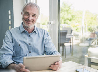 Happy senior man with tablet PC sitting at table - UUF26109