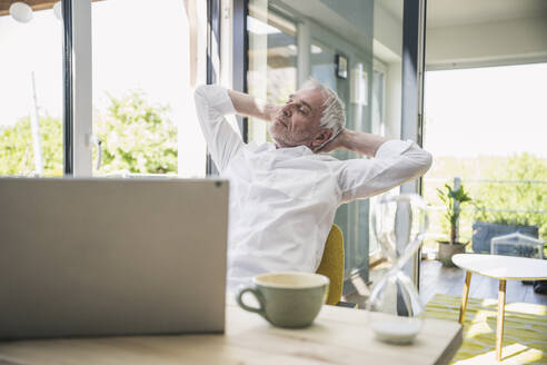 Businessman with hands behind head relaxing at home - UUF26117