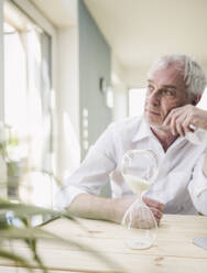 Hourglass on table with thoughtful senior man sitting in background - UUF26122
