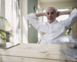 Hourglass on table with man in background at home - UUF26124