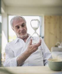 Retired senior man looking at hourglass - UUF26125