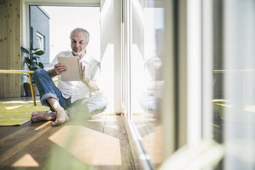 Senior man using tablet PC sitting on floor at home - UUF26127