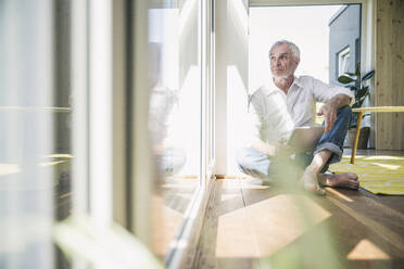 Senior man with tablet PC sitting on floor at home - UUF26128