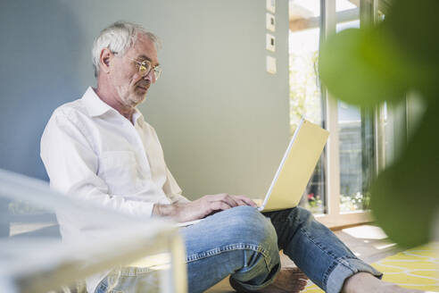 Älterer Mann mit Brille benutzt Laptop zu Hause - UUF26133