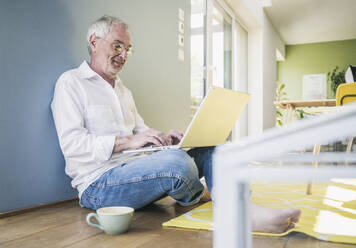 Lächelnder älterer Mann mit Brille, der zu Hause einen Laptop benutzt - UUF26134