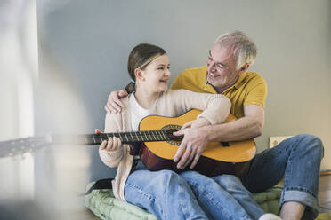 Happy girl with grandfather learning guitar at home - UUF26147