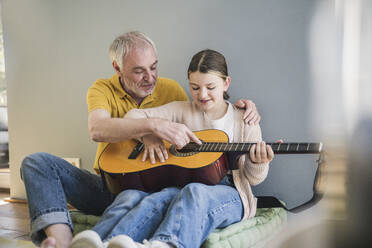 Happy senior man teaching guitar to granddaughter at home - UUF26148