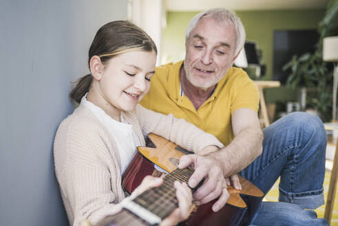 Lächelnder älterer Mann gibt seiner Enkelin zu Hause Gitarrenunterricht - UUF26149