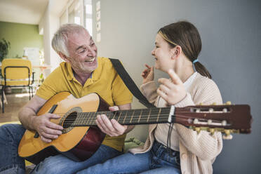 Glücklicher älterer Mann, der bei seiner Enkelin zu Hause Gitarre spielt - UUF26150