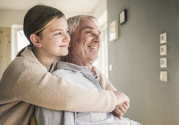 Smiling girl hugging grandfather from behind at home - UUF26151