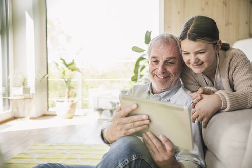 Glücklicher älterer Mann mit Enkelin bei der Nutzung eines Tablet-PCs zu Hause - UUF26162