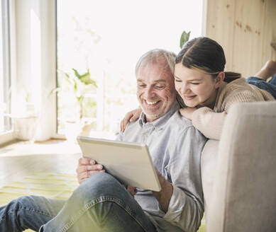 Glücklicher älterer Mann mit Enkelin bei der Nutzung eines Tablet-PCs zu Hause - UUF26164