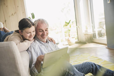 Smiling senior man with granddaughter using tablet PC at home - UUF26165