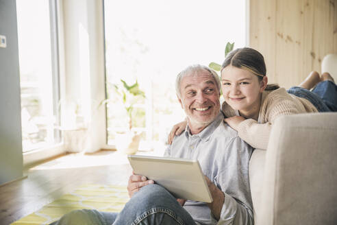 Lächelnder älterer Mann und Enkelin mit Tablet-PC zu Hause - UUF26167