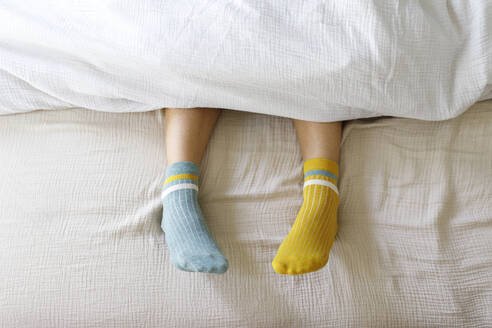 Woman wearing blue and yellow socks in bed at home - TYF00144