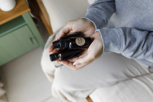 Woman holding essential oil bottles at home - TYF00147