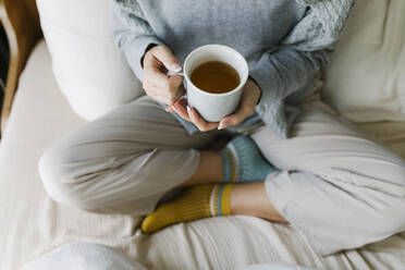 Hände einer Frau mit Teetasse auf dem Bett sitzend - TYF00151