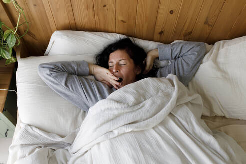Woman with eyes closed yawning in bed at home - TYF00155