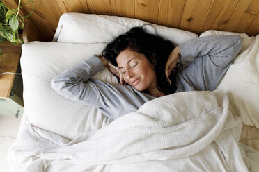 Lächelnde Frau streckt sich im Bett zu Hause - TYF00156
