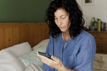 Frau mit Mobiltelefon auf dem Bett sitzend zu Hause - TYF00159