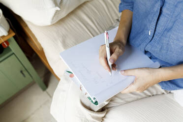 Woman writing in book sitting on bed at home - TYF00163