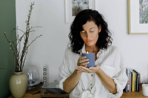 Woman with eyes closed holding candle in living room at home - TYF00173