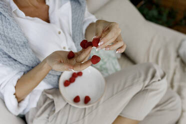Woman putting raspberries on fingers at home - TYF00178