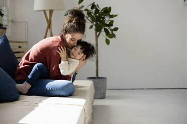 Mother and daughter hugging on sofa - JOSEF09403