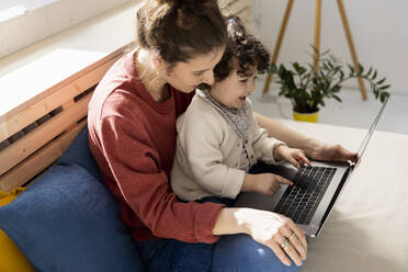 Kleines Mädchen mit Laptop auf dem Schoß der Mutter auf der Couch zu Hause - JOSEF09410