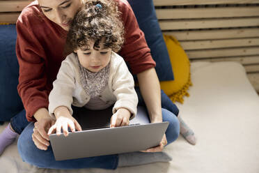 Little girl using laptop sitting on lap of mother on couch at home - JOSEF09411