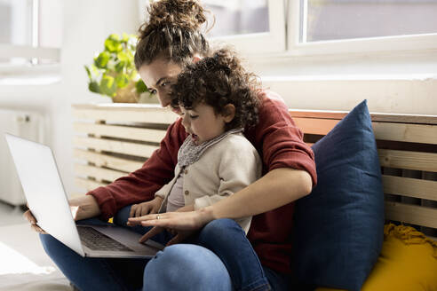 Kleines Mädchen mit Laptop auf dem Schoß der Mutter auf der Couch zu Hause - JOSEF09412