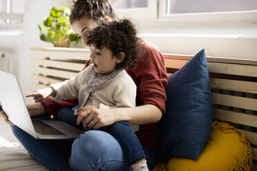 Kleines Mädchen mit Laptop auf dem Schoß der Mutter auf der Couch zu Hause - JOSEF09413