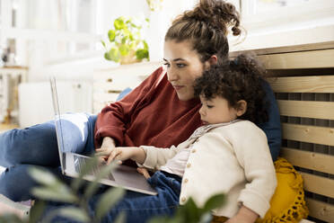 Little girl using laptop sitting on lap of mother on couch at home - JOSEF09415
