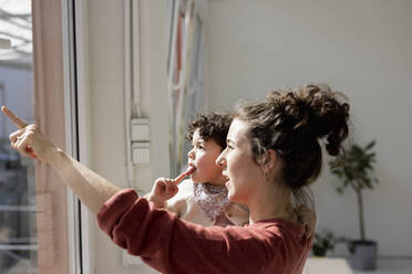 Mother carrying daughter pointing out of window - JOSEF09433