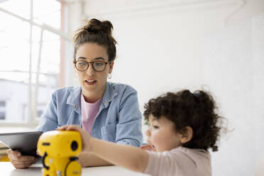 Arbeitende Mutter sitzt am Tisch Tochter spielt mit AI Spielzeugroboter - JOSEF09441