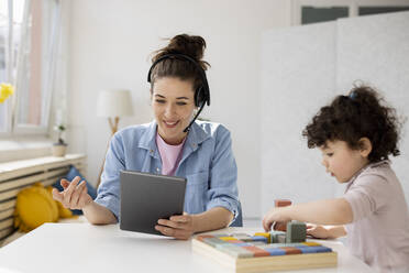 Mother working from home using digital tablet while daughter is playing with buiilding blocks - JOSEF09447