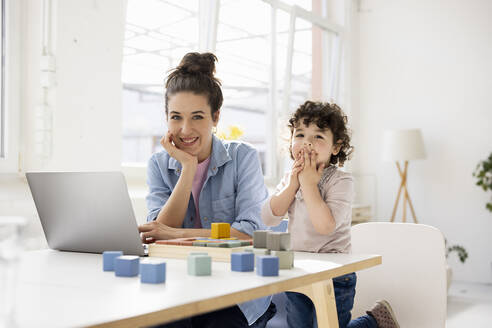 Mutter arbeitet von zu Hause aus am Laptop, während ihre Tochter mit Bauklötzen spielt - JOSEF09450