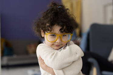 Cute little girl wearing oversized eyeglasses hugging self - JOSEF09482