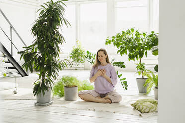 Woman sitting cross-legged amidst plants at home - SEAF00922