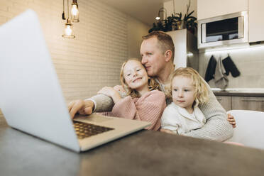 Lächelnder Geschäftsmann mit Töchtern, die zu Hause einen Laptop benutzen - SIF00096