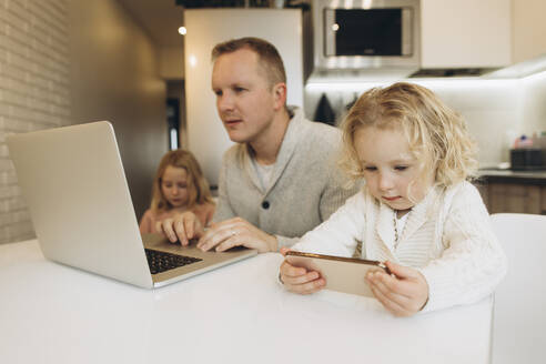 Tochter benutzt Smartphone, während der Vater zu Hause am Laptop arbeitet - SIF00101