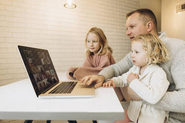 Businessman using laptop sitting with daughters at home - SIF00105