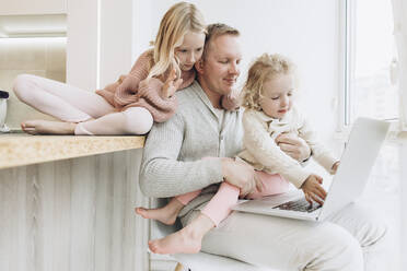 Töchter mit Vater, der zu Hause am Fenster sitzt und am Laptop arbeitet - SIF00122