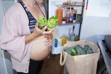 Pregnant woman putting away healthy groceries in kitchen - CAIF32376