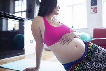 Pregnant woman in sports bra resting on yoga mat at home - CAIF32386