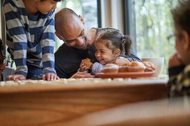 Glücklicher Vater und Tochter essen Muffin am Esstisch - CAIF32389