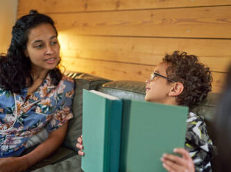 Mutter spricht mit Sohn mit Buch auf Sofa - CAIF32397